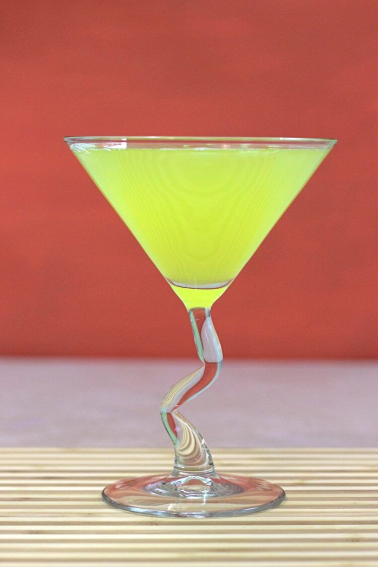 Bright yellow Algonquin Cocktail in front of dark orange background