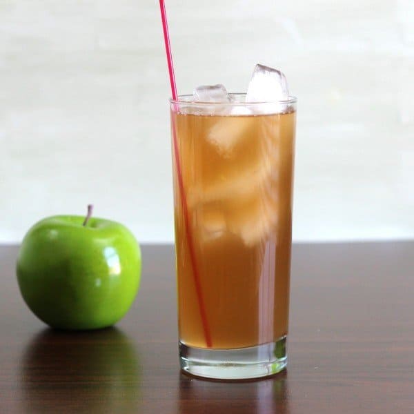 Full-length view of Apple Cart drink in tall glass with ice beside apple