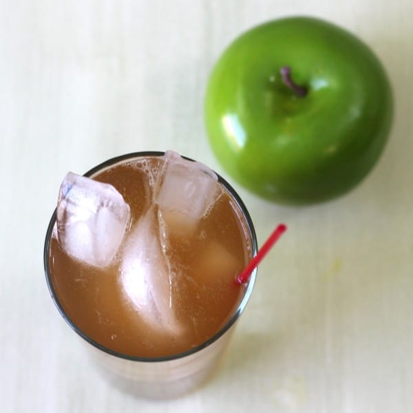 Overhead view of Apple Cart drink in tall glass with ice beside apple