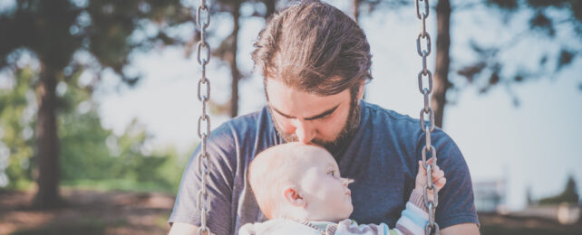 A bearded man kissing the top of baby's head.