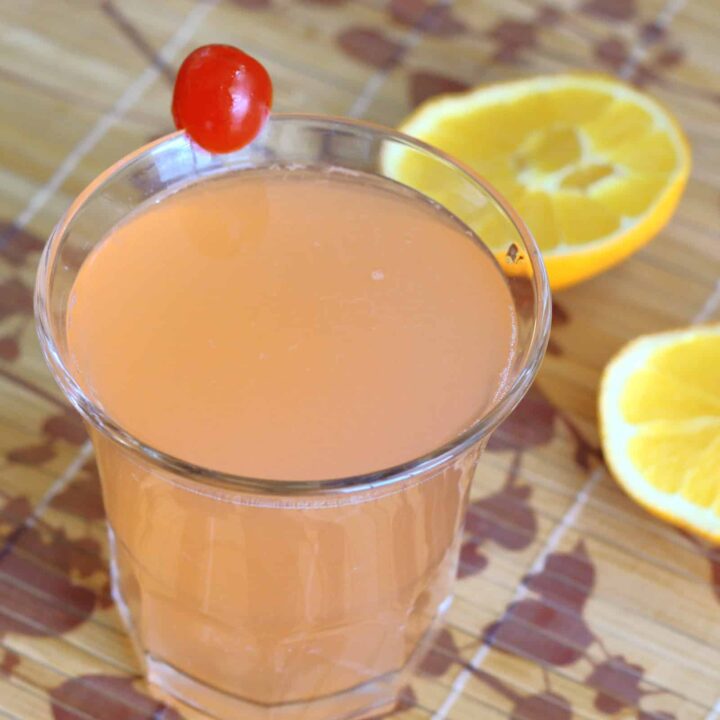 Blossom drink with cherry garnish and orange halves laying on table