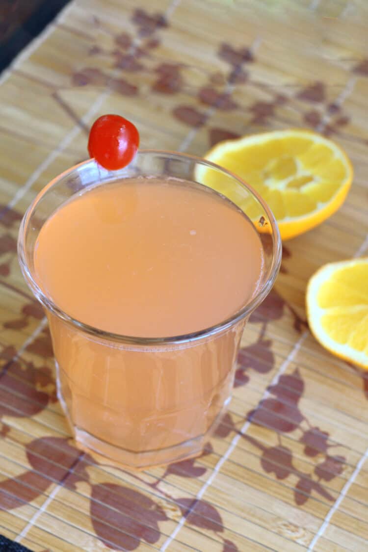 Blossom drink with cherry garnish and orange halves laying on table