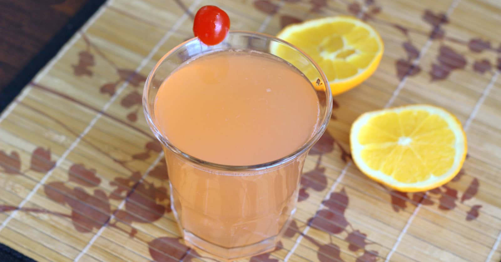 Blossom drink with cherry garnish and orange halves laying on table