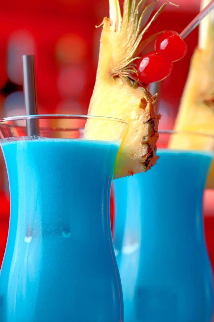 Two Blue Hawaiian drinks on bar with pineapple and cherry garnish