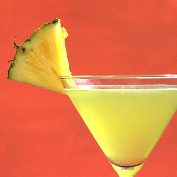 Closeup of Cabo drink with pineapple wedge against orange background