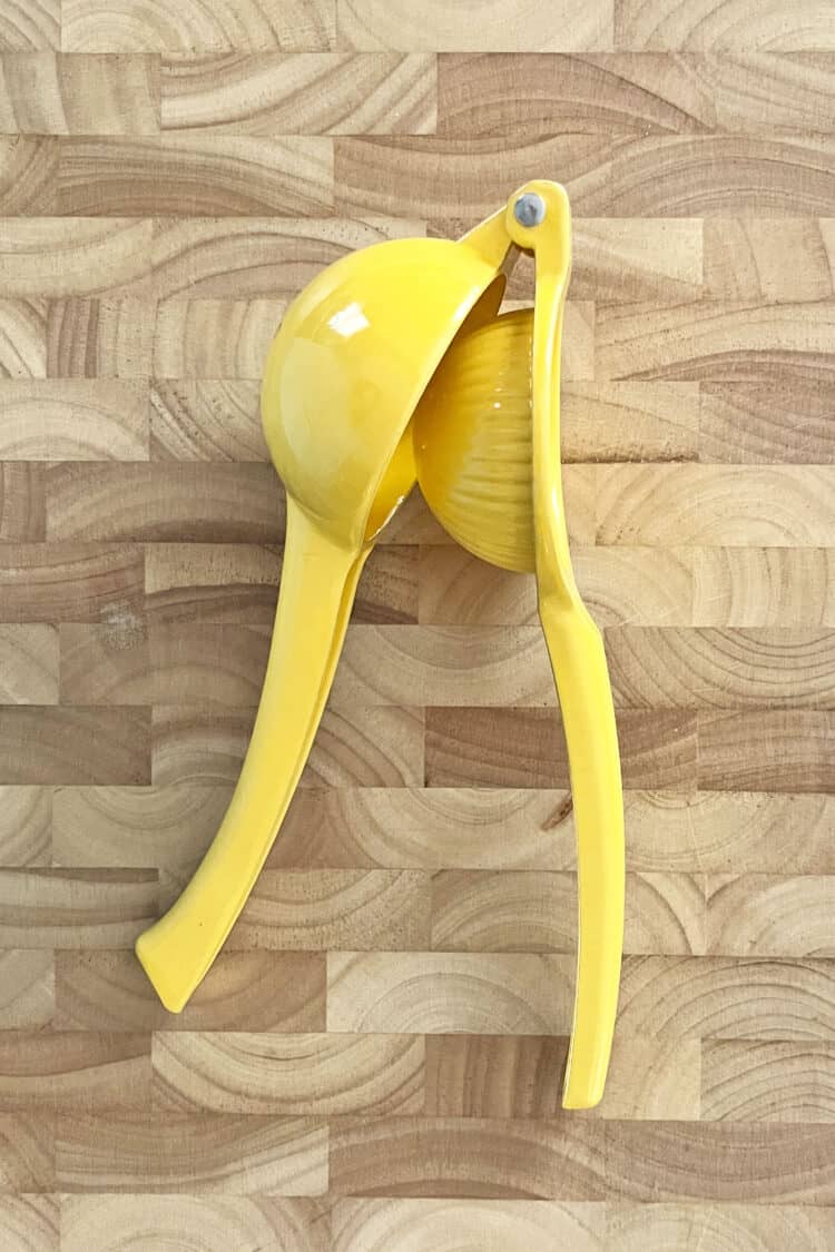 Yellow citrus squeezer on wooden cutting board