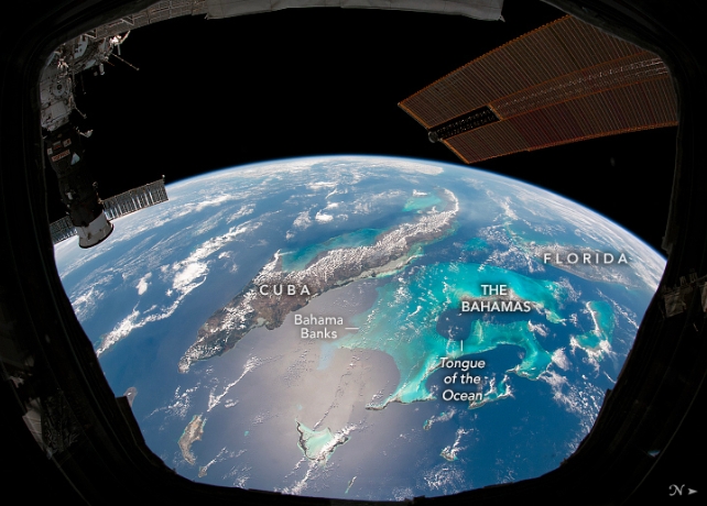 Part of Earth with clouds visible over the Caribbean Sea, in a dark image with the international space station visible in the top corners