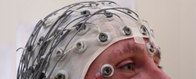 A cap holding electrodes in place on the top of a person's head, with eyes and nose visible