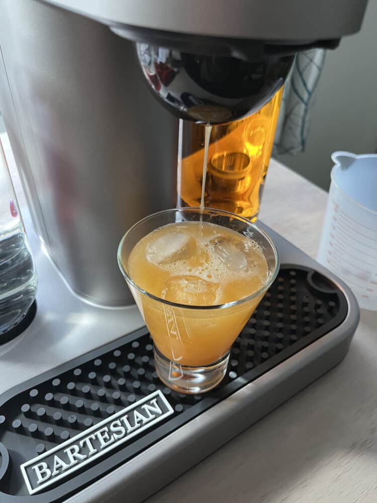 Finished cocktail being poured into glass of ice under dispenser