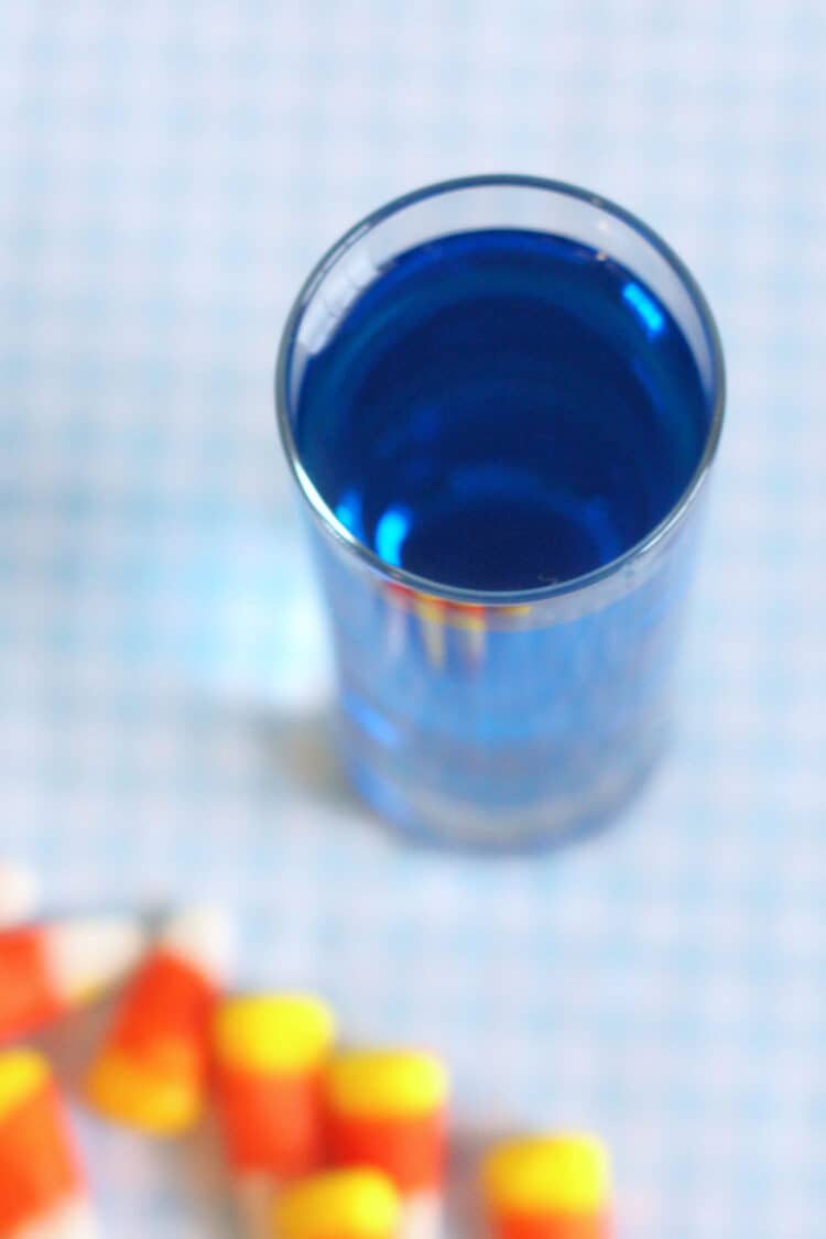 Bright blue cocktail in shot glass on table with candy corn