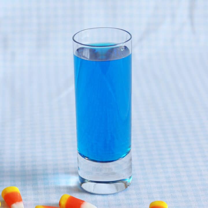 Bright blue cocktail in shot glass on table with candy corn