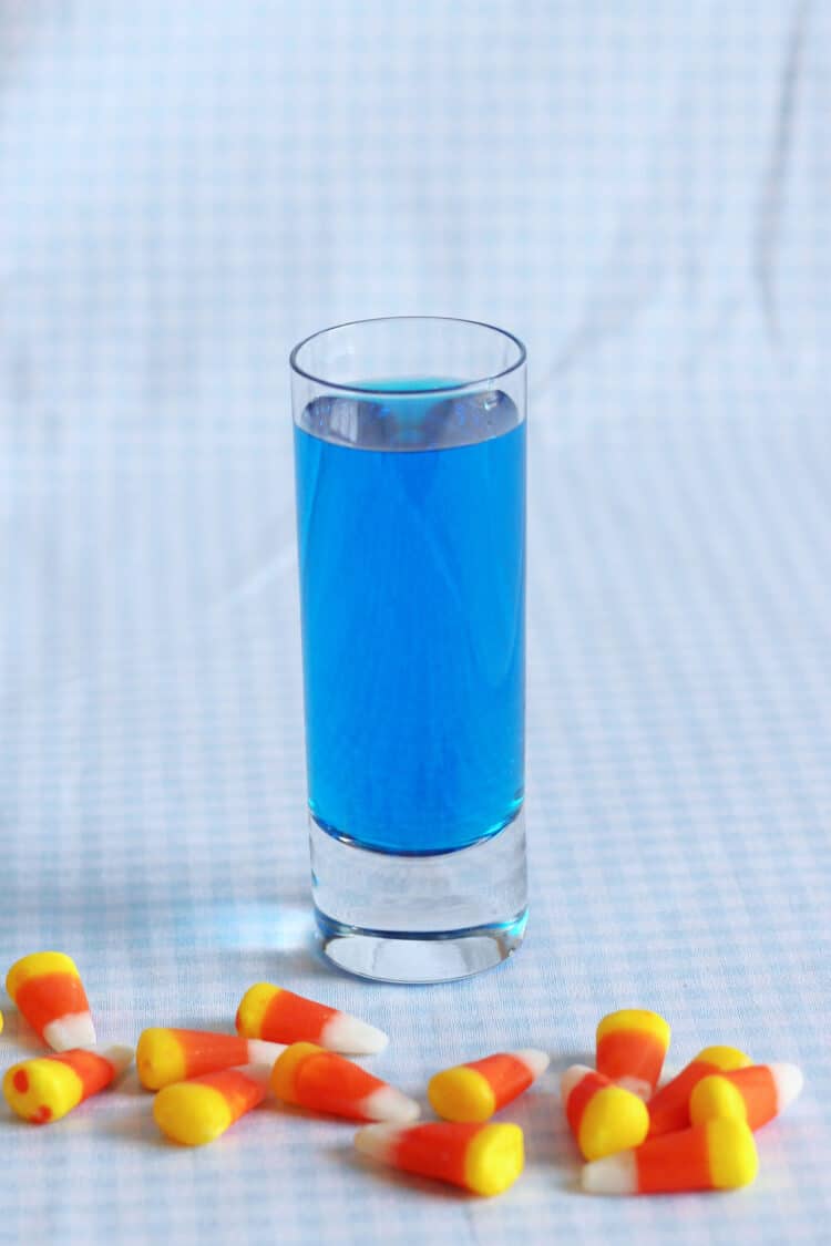 Bright blue cocktail in shot glass on table with candy corn