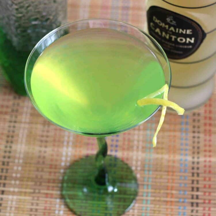 Overhead view of bright green cocktail in martini glass with lemon twist