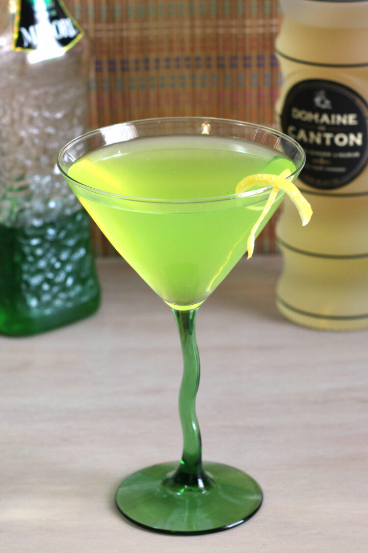 Bright green cocktail in martini glass with lemon twist