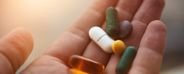 A human hand holding a variety of pills.