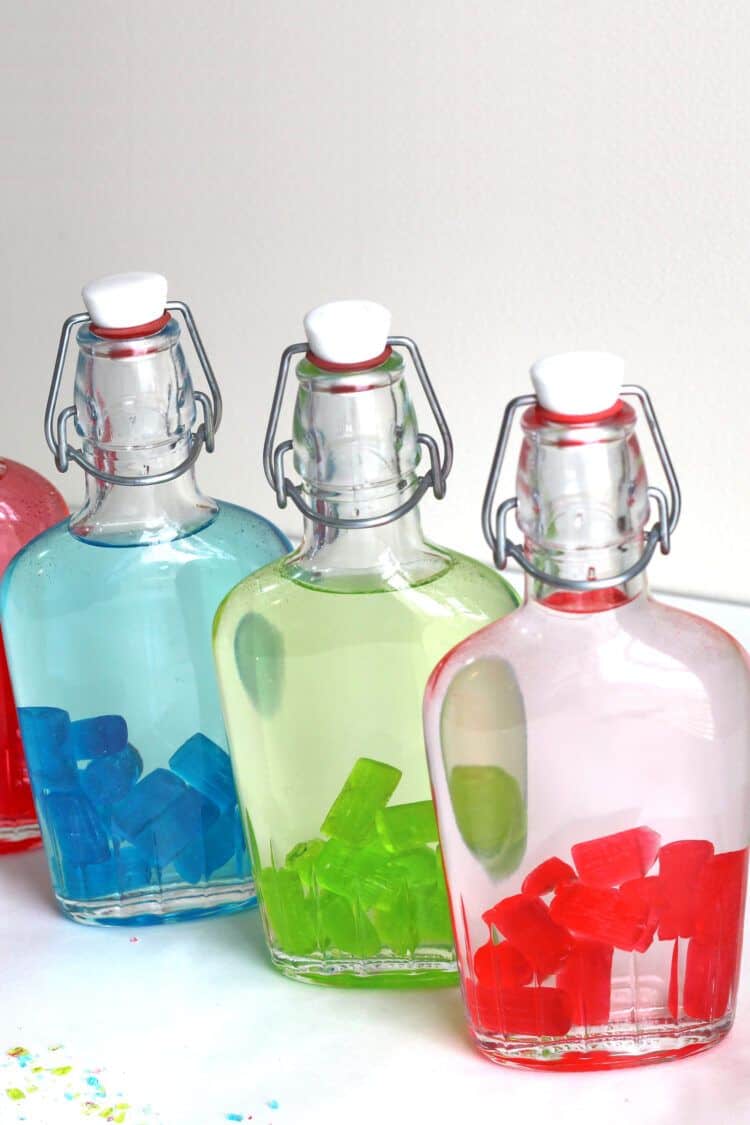 Closeup of Jolly Rancher candies starting to color the vodka in a flask