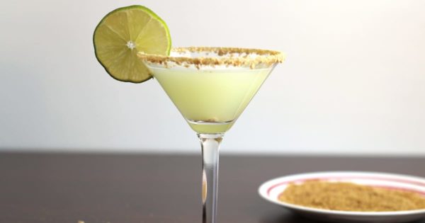 Pale green Key Lime Martini in glass with lime wheel and graham cracker crumb rim