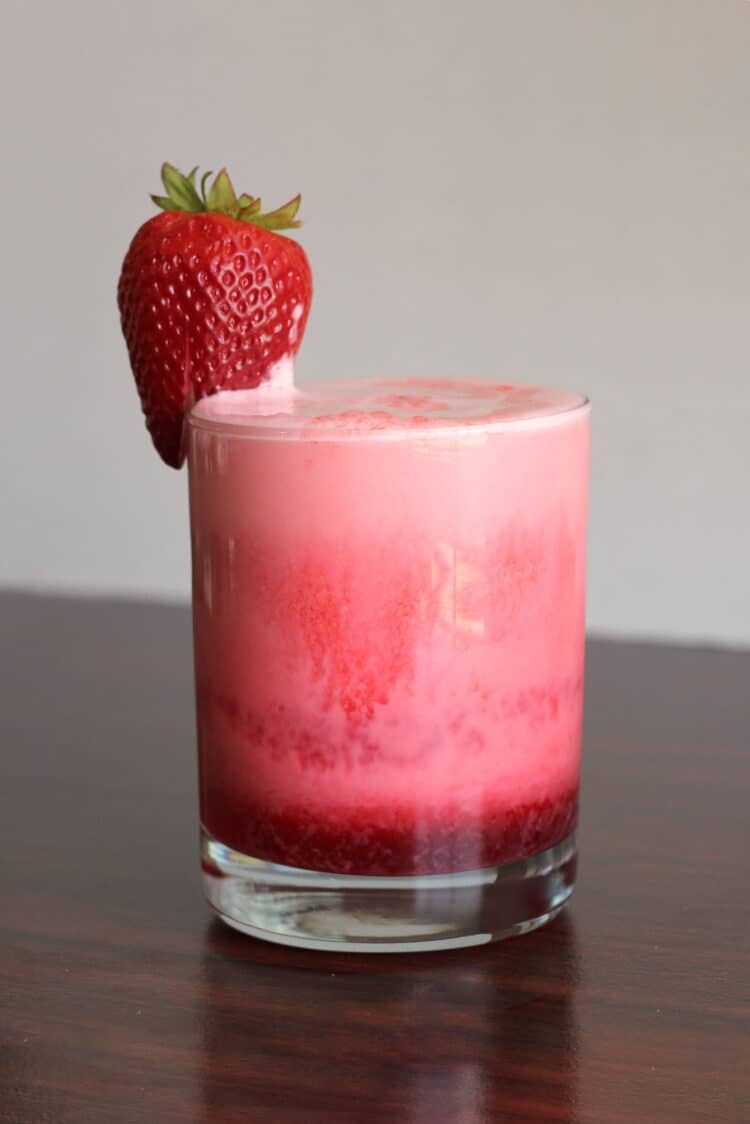 Pink and red cocktail in short tumbler with strawberry garnish