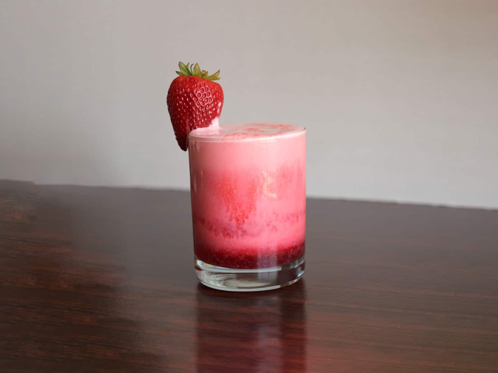 Pink and red cocktail in short tumbler with strawberry garnish