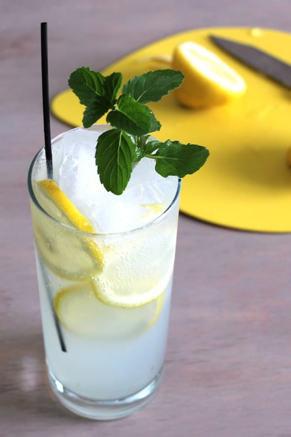 Limoncello Collins drink on table in front of cutting board with lemons