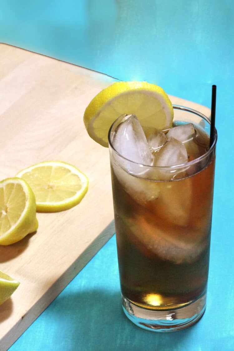 Long Island Iced Tea drink with lemon beside cutting board