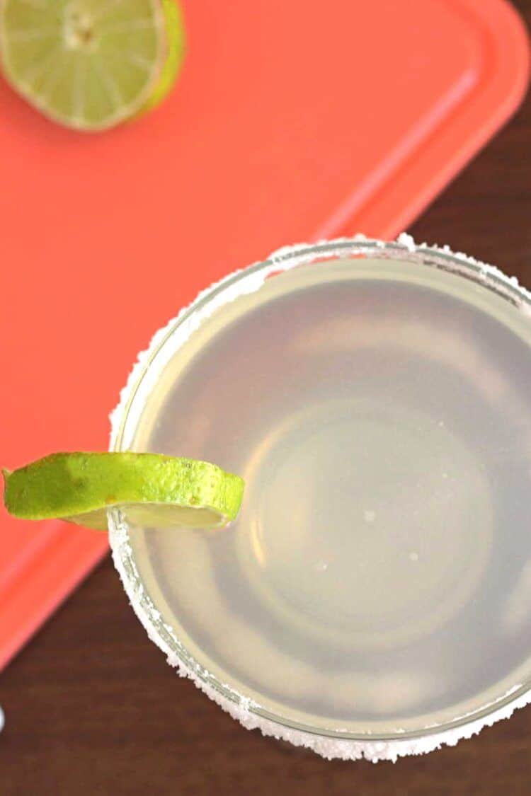 Overhead shot of margarita in glass beside cutting board with limes