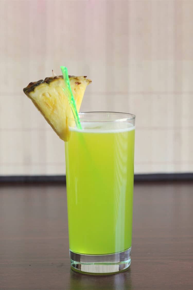 Bright green Monkey In a Tree drink with pineapple wedge garnish on table