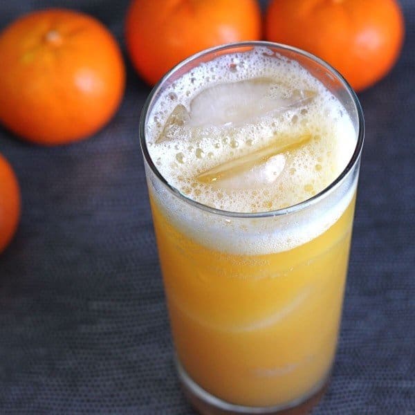 Angled overhead view of Orange Oasis cocktail in tall glass surrounded by oranges