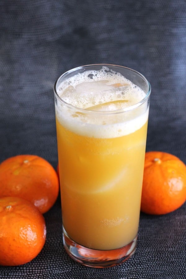 Orange Oasis cocktail in tall glass surrounded by oranges