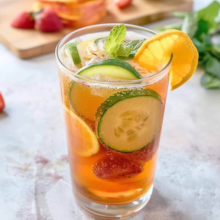 Pimm's Cup cocktail with fruit in glass beside sliced fruit on a cutting board