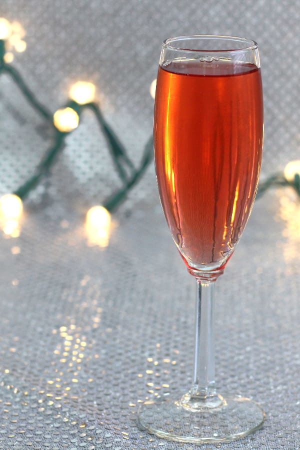 Poinsettia cocktail in champagne flute with Christmas lights in background