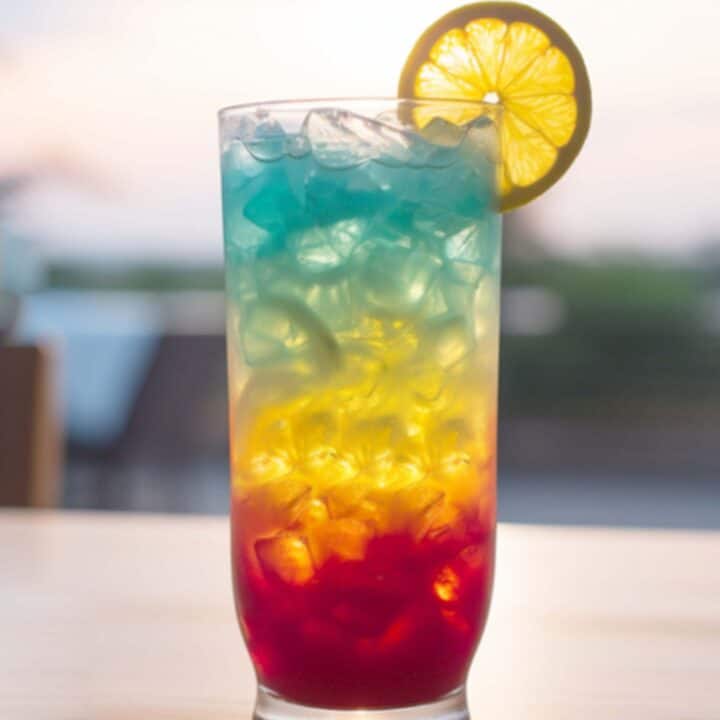 Rainbow Paradise cocktail on table in front of beach background