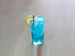 Bright blue Sex in the Driveway cocktail on table with lemon slice