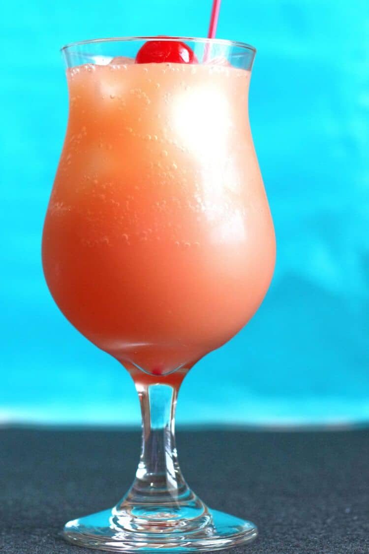 Sex on the Beach cocktail in hurricane glass with orange slice against beach background