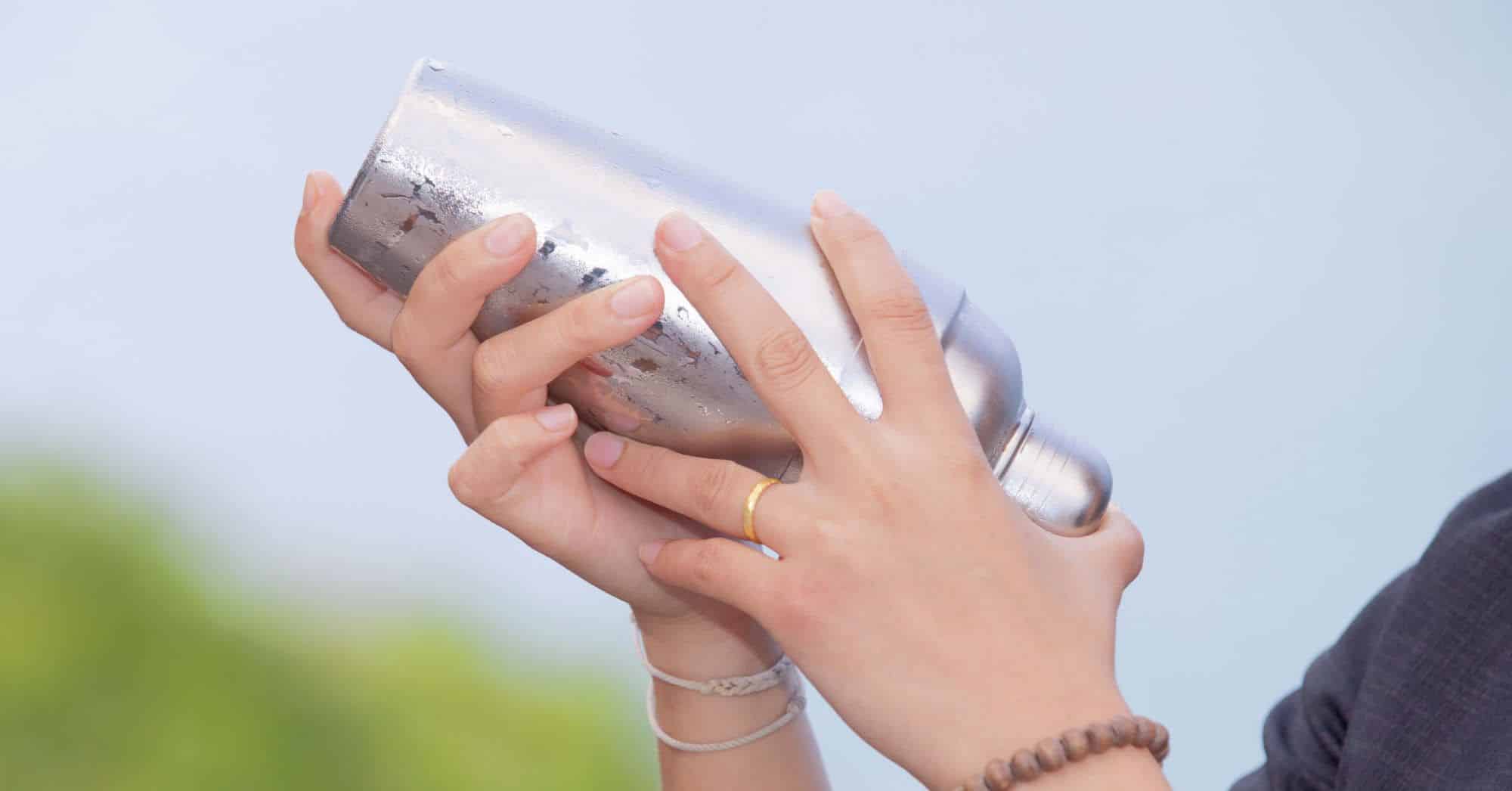 Woman's hands shaking cocktail silver shaker