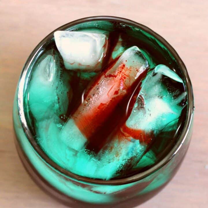 The Shark Bite cocktail recipe gets its name from the way the drops of grenadine look like blood in greenish-blue water. This one always gets a laugh at parties, especially Halloween parties. This is a fun, fruity drink that impresses guests and tastes delicious. #drinkrecipes #rumdrinks #rumcocktails #partydrinks #cocktailrecipes #partycocktails