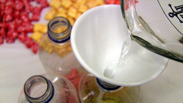 Pouring vodka through a funnel into a water bottle containing Starbursts