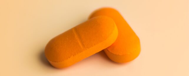 Two oval shaped orange pills with a dividing line, on a lighter orange background.